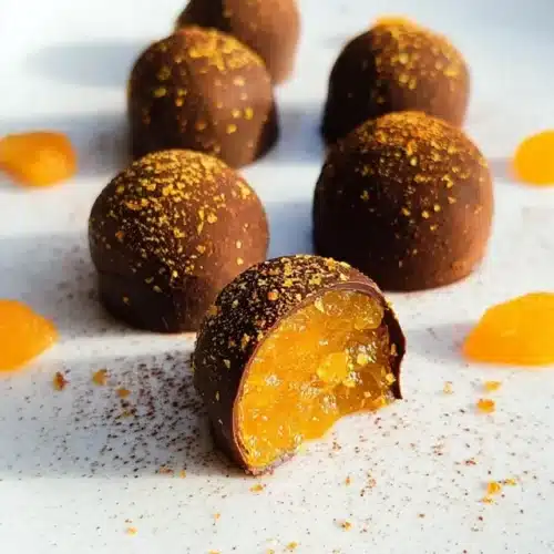 Truffes chocolat noir garnies de confit d’abricot et ganache, décorées de beurre de cacao coloré.
